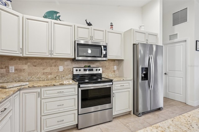 kitchen featuring stainless steel appliances, light stone counters, white cabinets, and backsplash