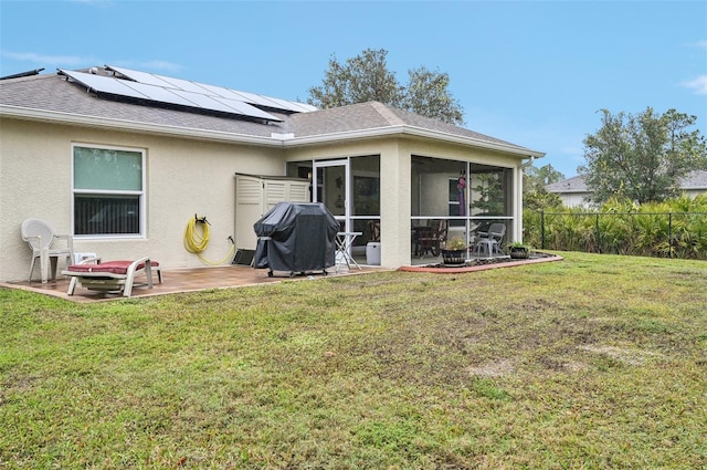 back of house with a lawn, a patio area, a sunroom, and solar panels