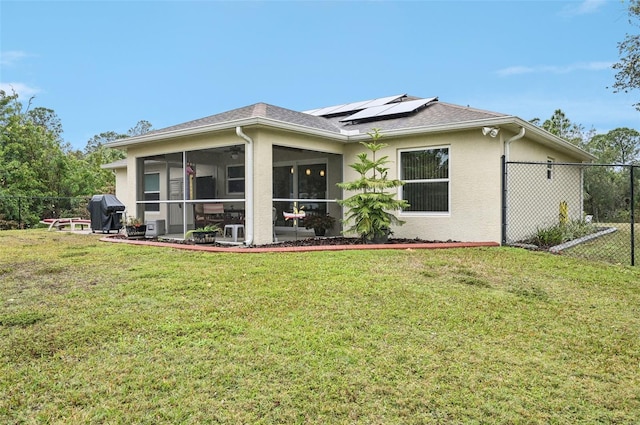 back of house featuring a sunroom, a lawn, and solar panels