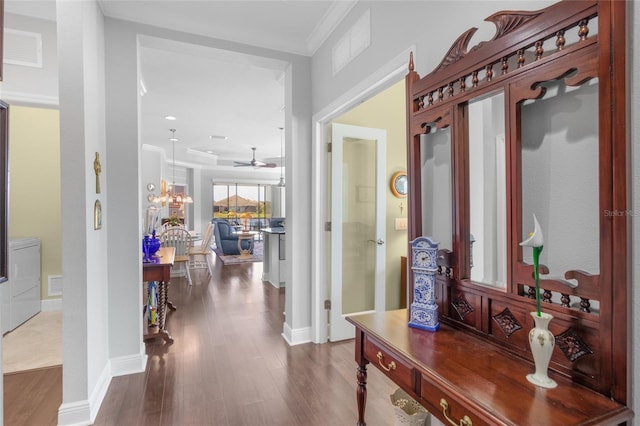 hallway featuring washer / dryer, hardwood / wood-style floors, crown molding, and a notable chandelier