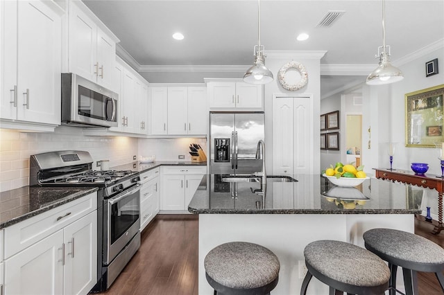 kitchen with dark stone countertops, appliances with stainless steel finishes, a kitchen island with sink, and white cabinets