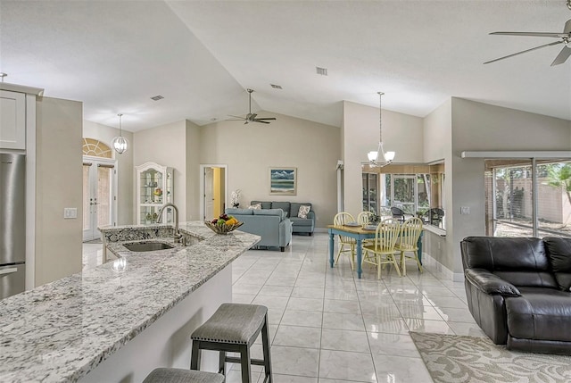 kitchen featuring light stone countertops, sink, ceiling fan with notable chandelier, hanging light fixtures, and vaulted ceiling