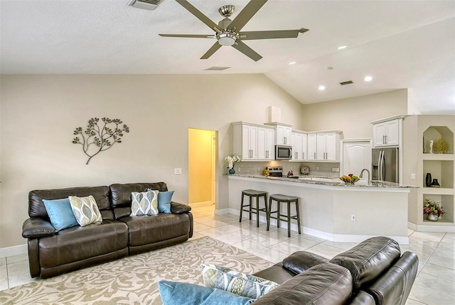 living room featuring high vaulted ceiling, sink, light tile patterned floors, and ceiling fan