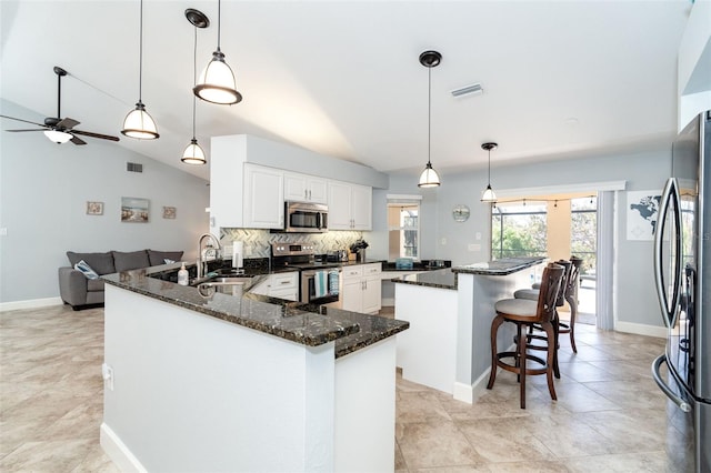 kitchen with appliances with stainless steel finishes, pendant lighting, dark stone counters, and kitchen peninsula