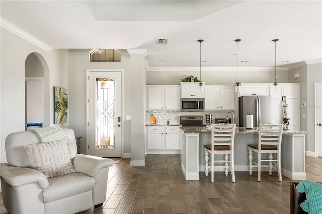 kitchen with pendant lighting, a center island with sink, dark wood-type flooring, white cabinetry, and stainless steel appliances