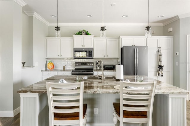 kitchen featuring a kitchen island with sink, pendant lighting, a kitchen breakfast bar, appliances with stainless steel finishes, and white cabinetry