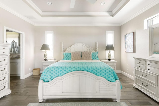 bedroom with ceiling fan, dark hardwood / wood-style floors, ensuite bath, a tray ceiling, and ornamental molding