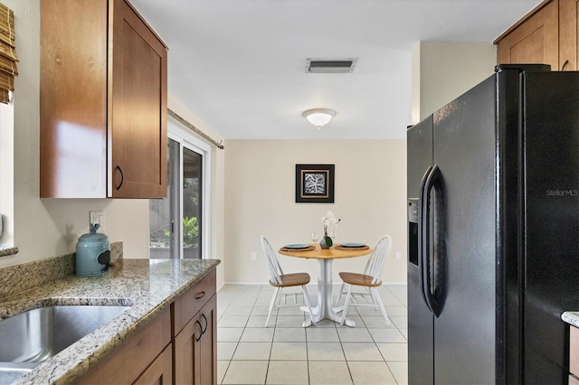 kitchen with sink, light stone countertops, light tile patterned floors, and black fridge