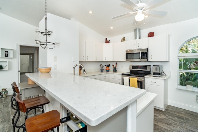 kitchen with appliances with stainless steel finishes, kitchen peninsula, white cabinetry, vaulted ceiling, and dark hardwood / wood-style floors