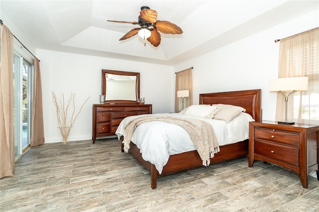 bedroom featuring ceiling fan, hardwood / wood-style flooring, multiple windows, and a raised ceiling