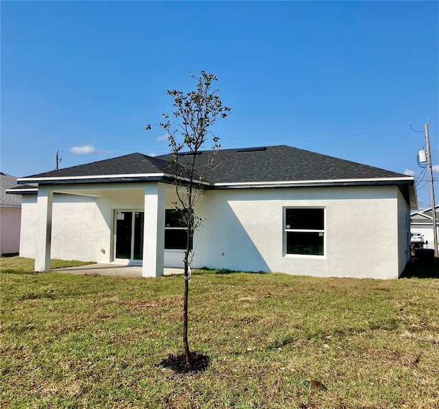 back of house featuring a patio area, roof with shingles, a lawn, and stucco siding