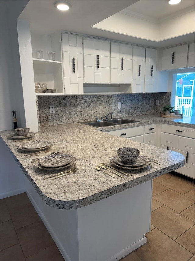 kitchen featuring tasteful backsplash, white cabinetry, sink, tile patterned flooring, and kitchen peninsula