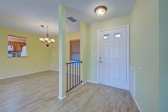 foyer with a notable chandelier, a textured ceiling, and light hardwood / wood-style flooring