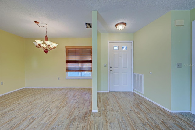 entryway with a notable chandelier, a textured ceiling, and light hardwood / wood-style flooring