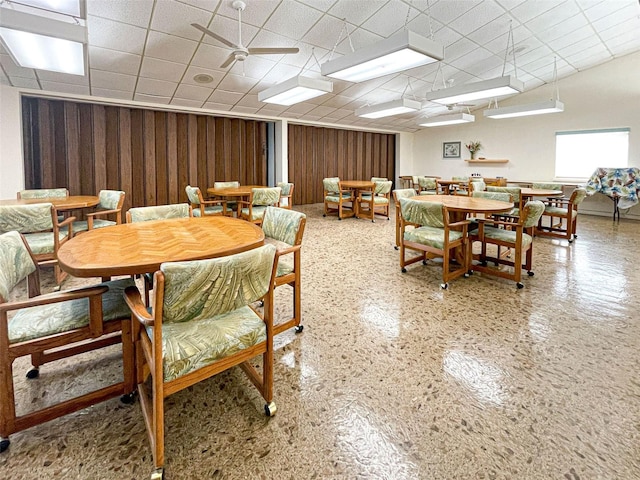 dining space featuring a drop ceiling, wooden walls, and ceiling fan