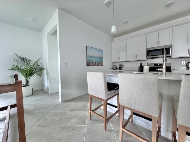 kitchen with light tile patterned floors, a breakfast bar, white cabinetry, pendant lighting, and stainless steel appliances