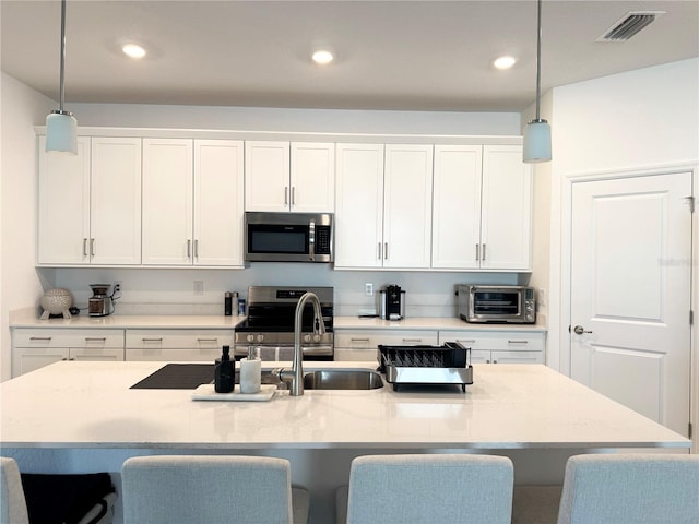 kitchen featuring stainless steel appliances, decorative light fixtures, and a kitchen island with sink