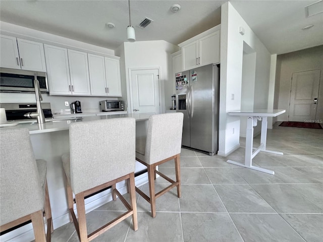 kitchen featuring white cabinets, light tile patterned floors, a breakfast bar, decorative light fixtures, and stainless steel appliances