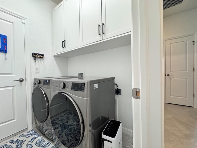 laundry room with light tile patterned flooring, cabinets, and washing machine and clothes dryer