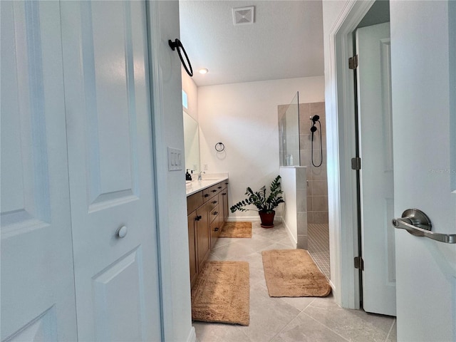 bathroom with a tile shower, tile patterned floors, a textured ceiling, and vanity