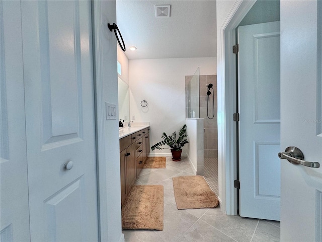 bathroom with a tile shower, a textured ceiling, tile patterned flooring, and vanity