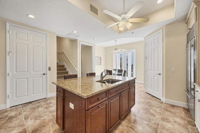 kitchen with sink, light tile patterned floors, ceiling fan, light stone countertops, and an island with sink