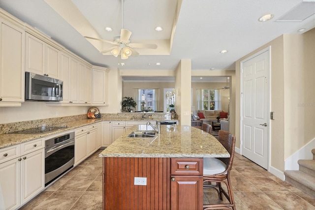 kitchen featuring a raised ceiling, sink, a kitchen bar, a kitchen island with sink, and stainless steel appliances