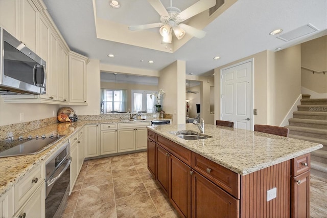 kitchen featuring appliances with stainless steel finishes, a tray ceiling, sink, and a center island with sink