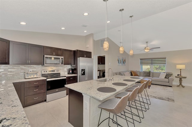 kitchen featuring a breakfast bar, light stone countertops, stainless steel appliances, sink, and decorative light fixtures