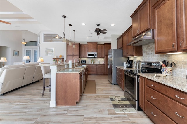 kitchen with an island with sink, a kitchen breakfast bar, backsplash, stainless steel appliances, and decorative light fixtures