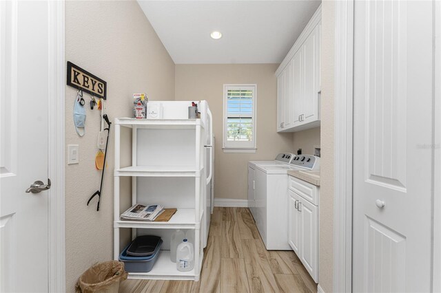 laundry area featuring washer and clothes dryer, light hardwood / wood-style floors, and cabinets