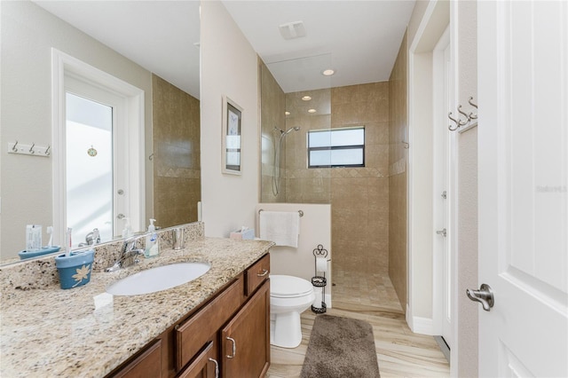 bathroom featuring vanity, a tile shower, hardwood / wood-style flooring, and toilet