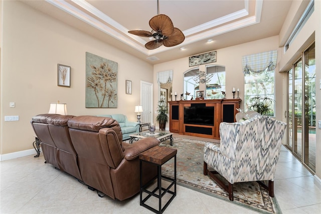 tiled living room featuring a fireplace, ceiling fan, crown molding, and a tray ceiling