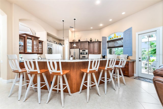 kitchen featuring a kitchen bar, kitchen peninsula, hanging light fixtures, light stone countertops, and appliances with stainless steel finishes