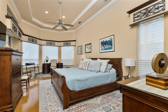 bedroom with ornamental molding, light wood-type flooring, ceiling fan, and a tray ceiling