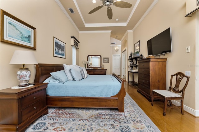 bedroom with light hardwood / wood-style floors, ceiling fan, crown molding, and a tray ceiling