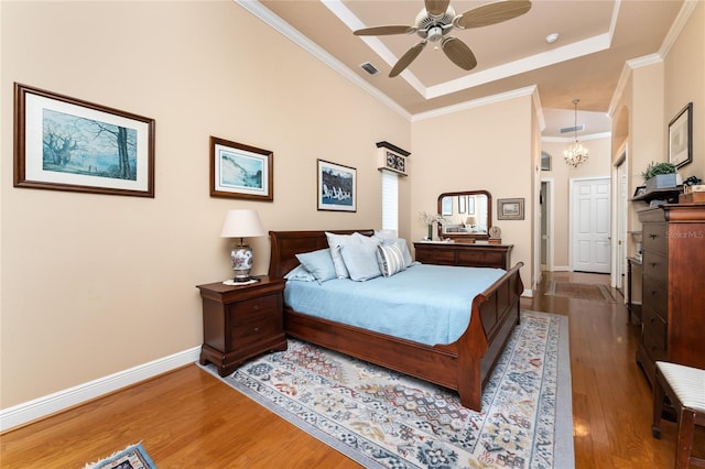 bedroom featuring ornamental molding, hardwood / wood-style floors, ceiling fan with notable chandelier, and a raised ceiling