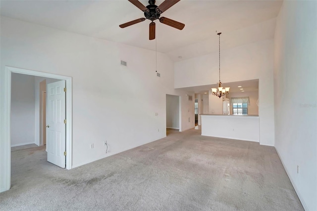 unfurnished living room with ceiling fan with notable chandelier, high vaulted ceiling, and light colored carpet