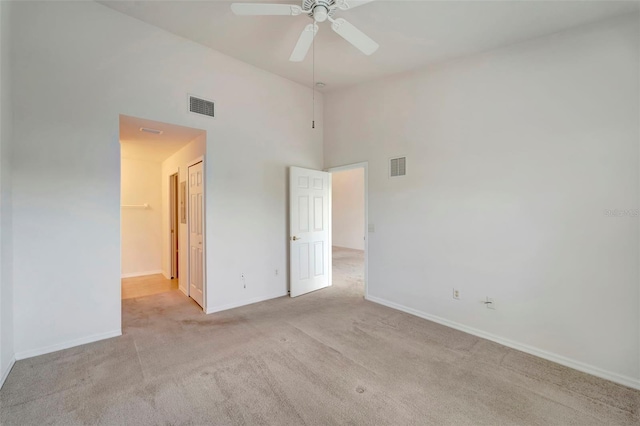 carpeted empty room with a towering ceiling and ceiling fan