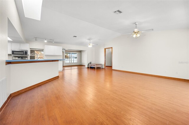 unfurnished living room with ceiling fan, track lighting, vaulted ceiling, and light wood-type flooring