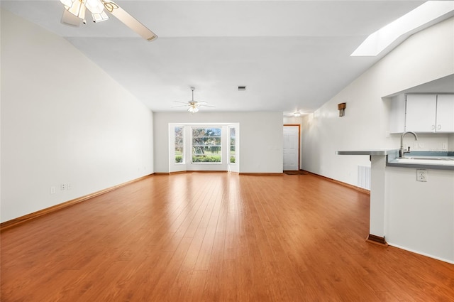 unfurnished living room with lofted ceiling with skylight, sink, light wood-type flooring, and ceiling fan