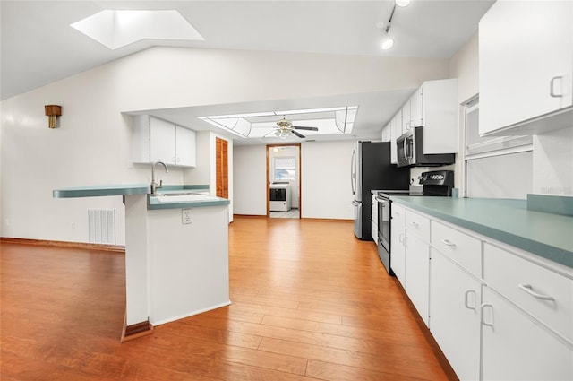 kitchen featuring white cabinetry, vaulted ceiling with skylight, sink, light hardwood / wood-style floors, and stainless steel appliances