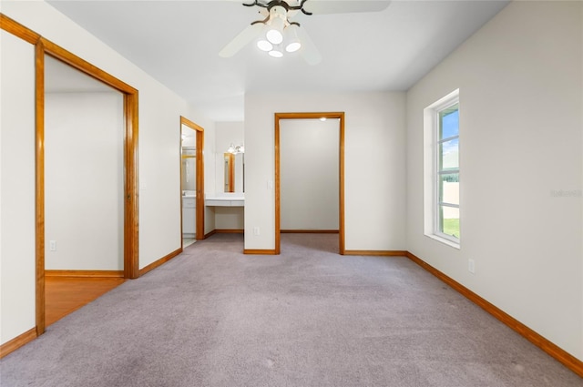 unfurnished bedroom featuring a closet, ensuite bath, light colored carpet, and ceiling fan