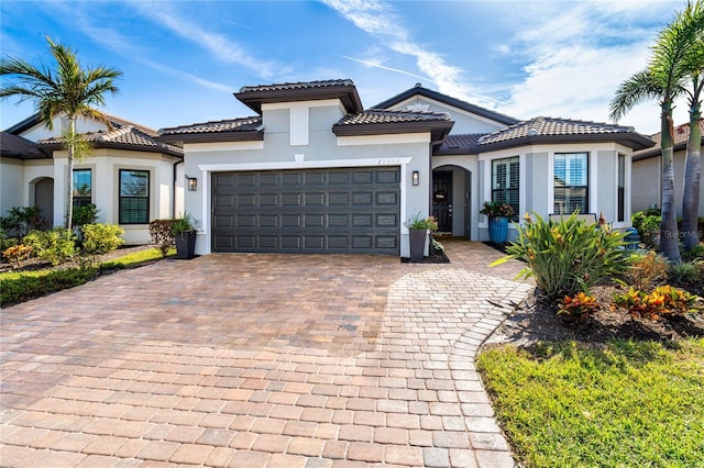 mediterranean / spanish house featuring decorative driveway, a tiled roof, an attached garage, and stucco siding