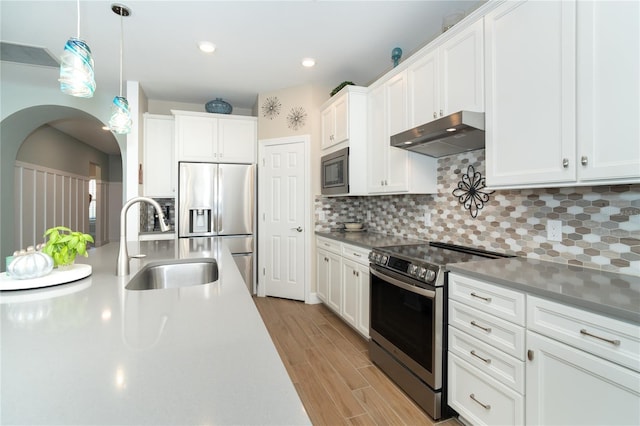 kitchen with appliances with stainless steel finishes, white cabinetry, sink, decorative backsplash, and hanging light fixtures