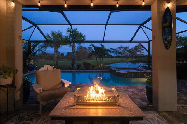 pool at dusk with an in ground hot tub, a patio, glass enclosure, and an outdoor fire pit