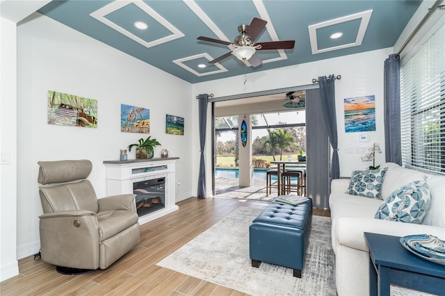 living area with a ceiling fan, a glass covered fireplace, a sunroom, wood finished floors, and baseboards