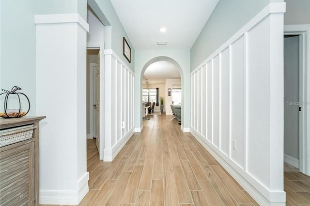 corridor featuring arched walkways, wood finish floors, and baseboards