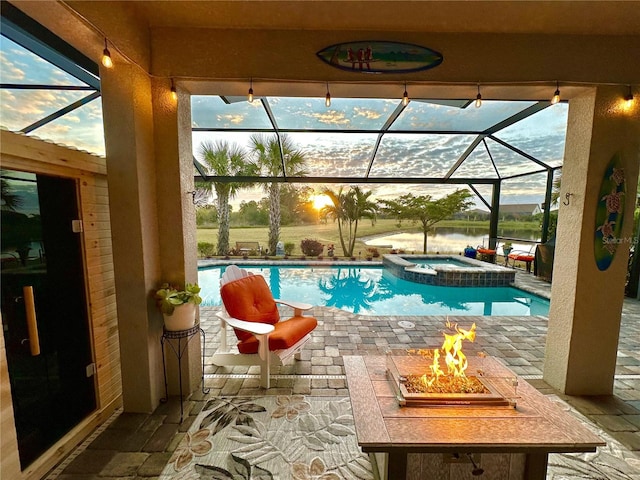 view of pool featuring a patio, a pool with connected hot tub, a water view, glass enclosure, and a fire pit