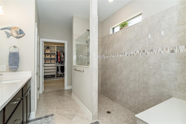 bathroom with a walk in closet, vanity, baseboards, and a walk in shower